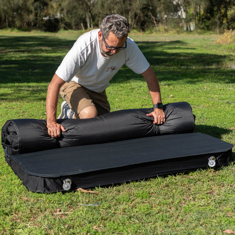 Load image into Gallery viewer, Rolling up a Quest Dreamlite camping mattress on grass

