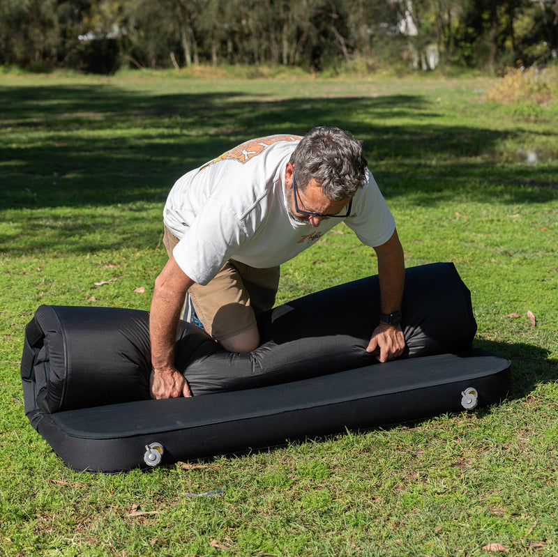 Load image into Gallery viewer, Rolling up a Quest Dreamlite camping mattress on grass
