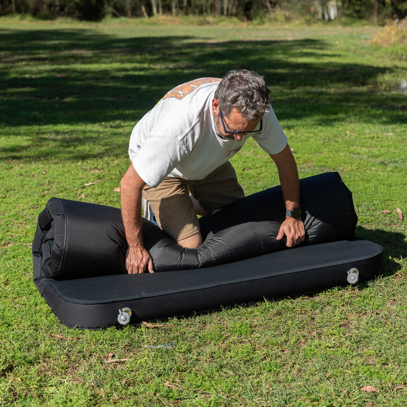 Load image into Gallery viewer, Rolling up a Quest Dreamlite camping mattress on grass

