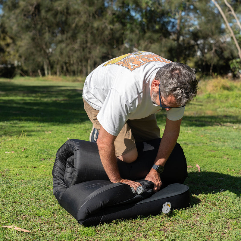 Load image into Gallery viewer, Rolling up a Quest Dreamlite camping mattress on grass
