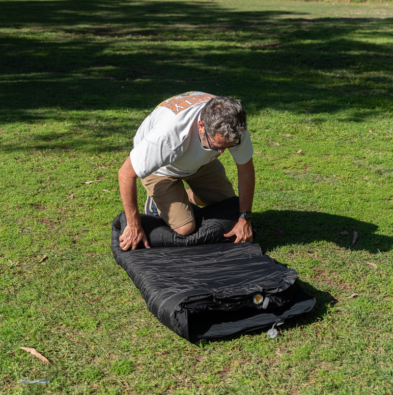 Load image into Gallery viewer, Rolling up a Quest Dreamlite camping mattress on grass
