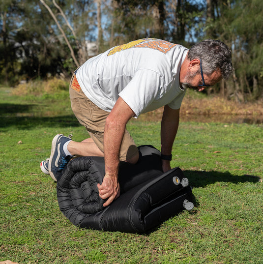 Rolling up a Quest Dreamlite camping mattress on grass