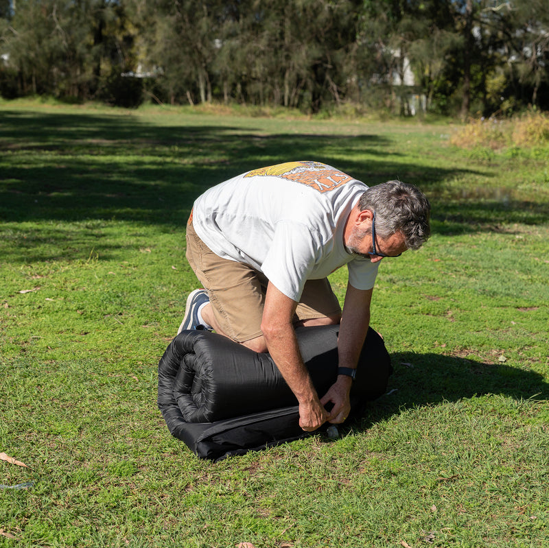 Load image into Gallery viewer, Rolling up a Quest Dreamlite camping mattress on grass
