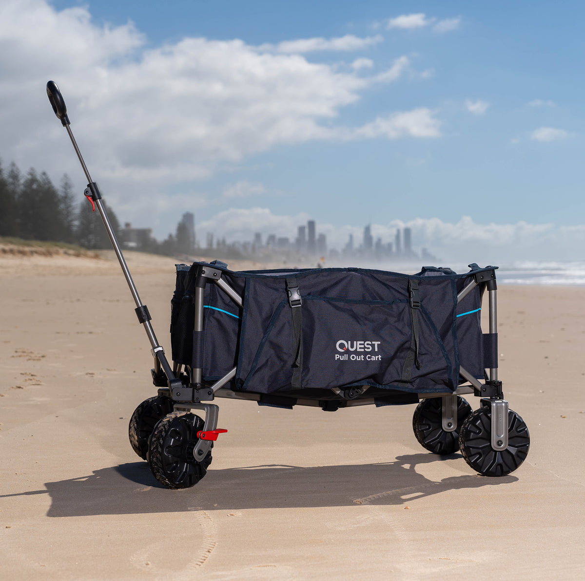 Folding cart trolley wagon with Quest branding on a sandy beach with a city skyline in the background.