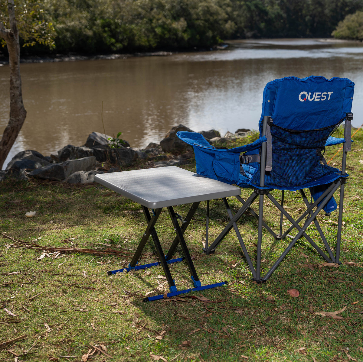 Big Mutha camping chair with 'Quest' branding next to a  Micro Pack Multi Height folding table by a body of water.

