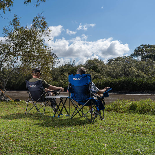 Two people sitting in 'Quest' branded camping chairs outdoors with Micro Pack Side Table